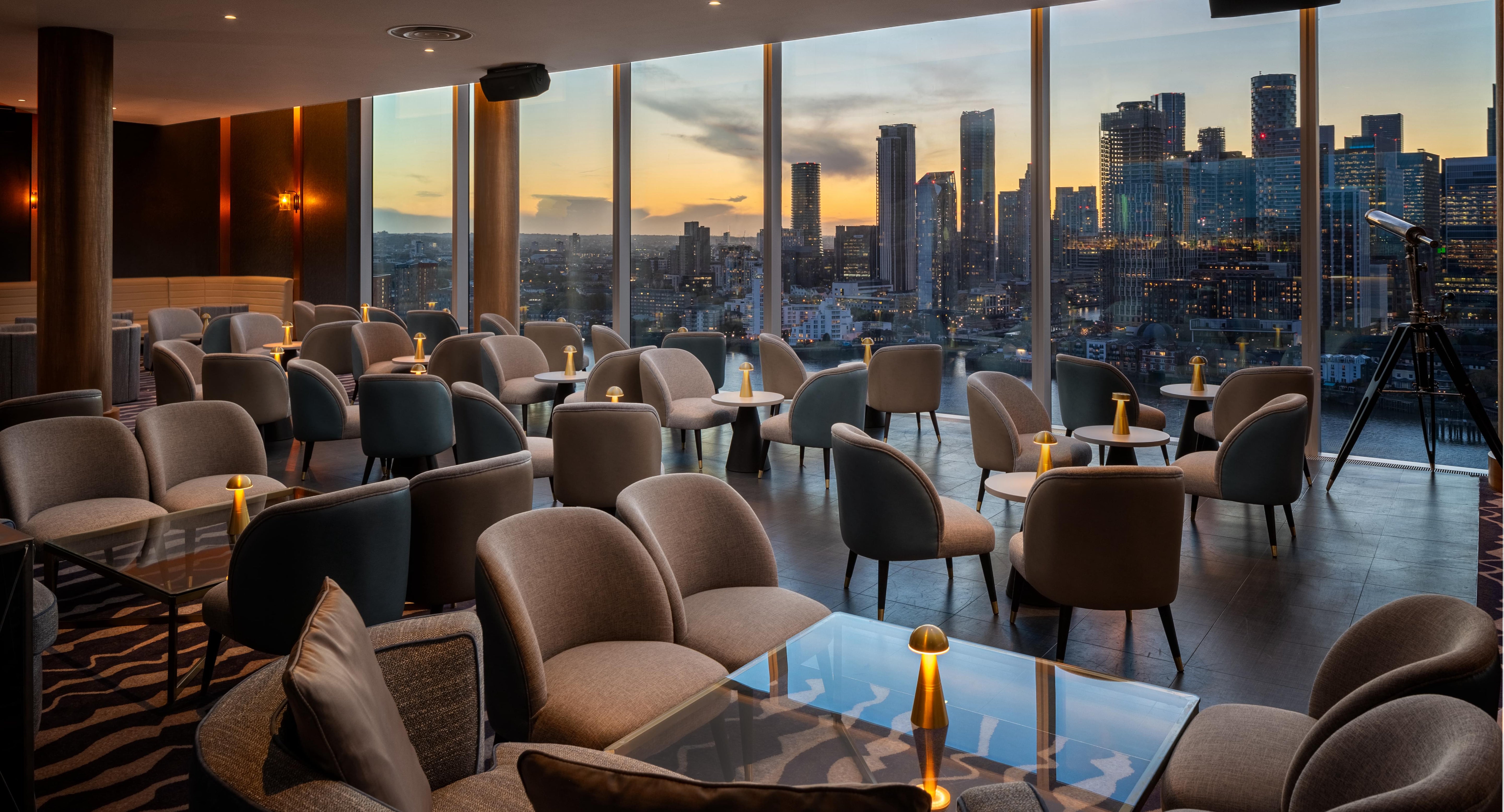 Modern restaurant interior with cordless table lamps on the tables and a city skyline view during sunset.