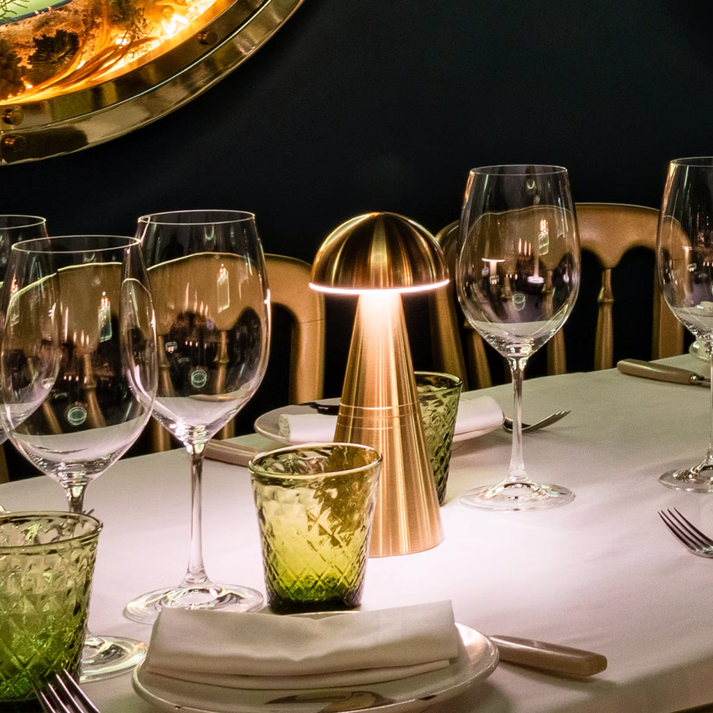 Rechargeable table lamp in Brass on a fine dining restaurant table with gold chairs and white table cloth.