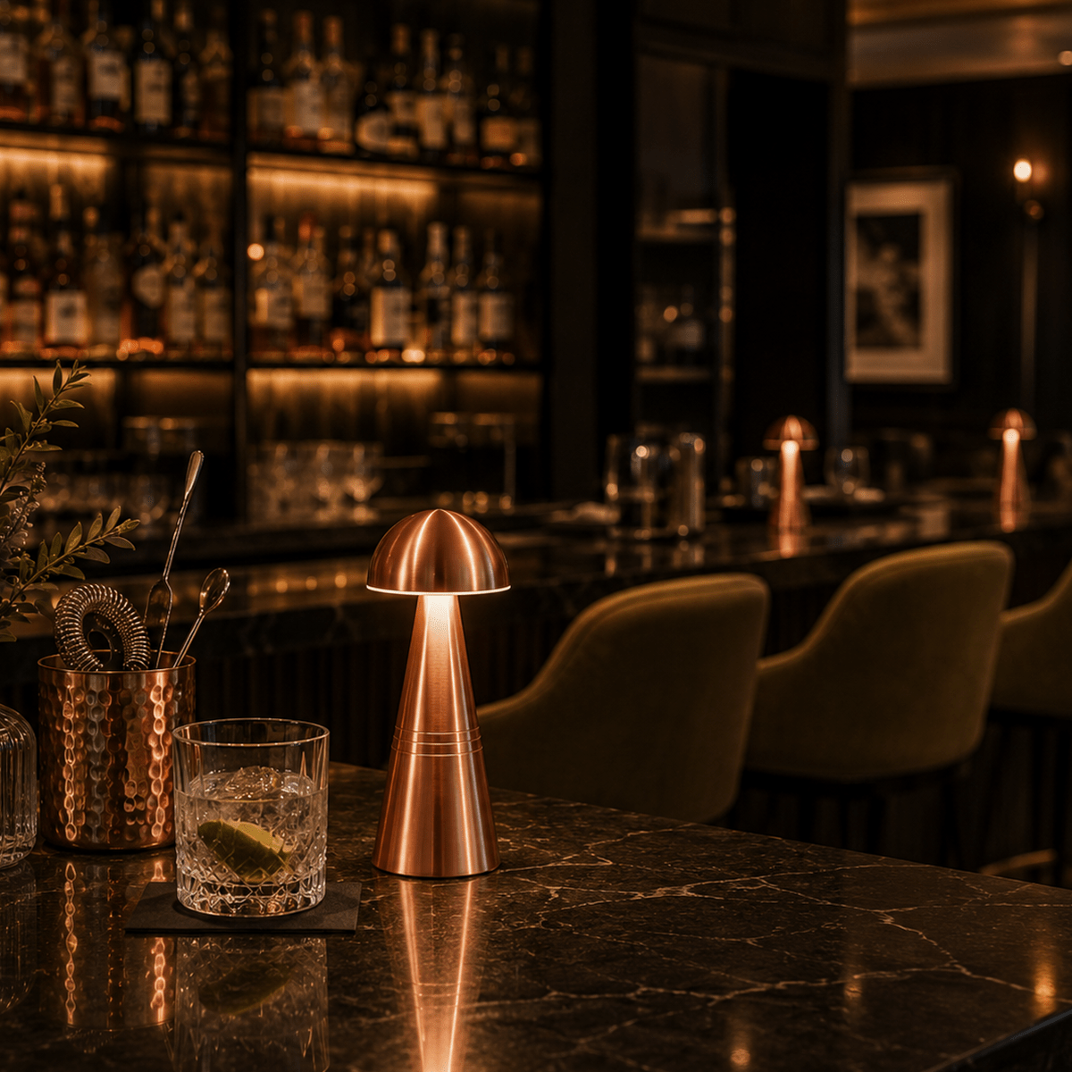 Copper rechargable lamp and glass on a bar counter with a dimly lit bar in the background