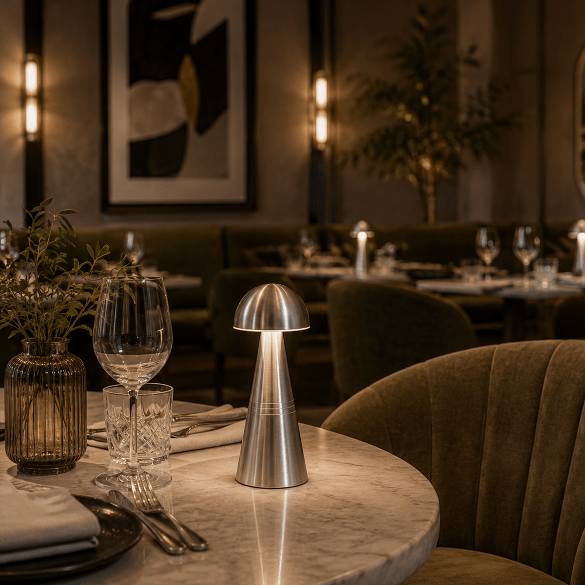 Dining table setting in a restaurant with a cordless lamp, glasses, and cutlery.