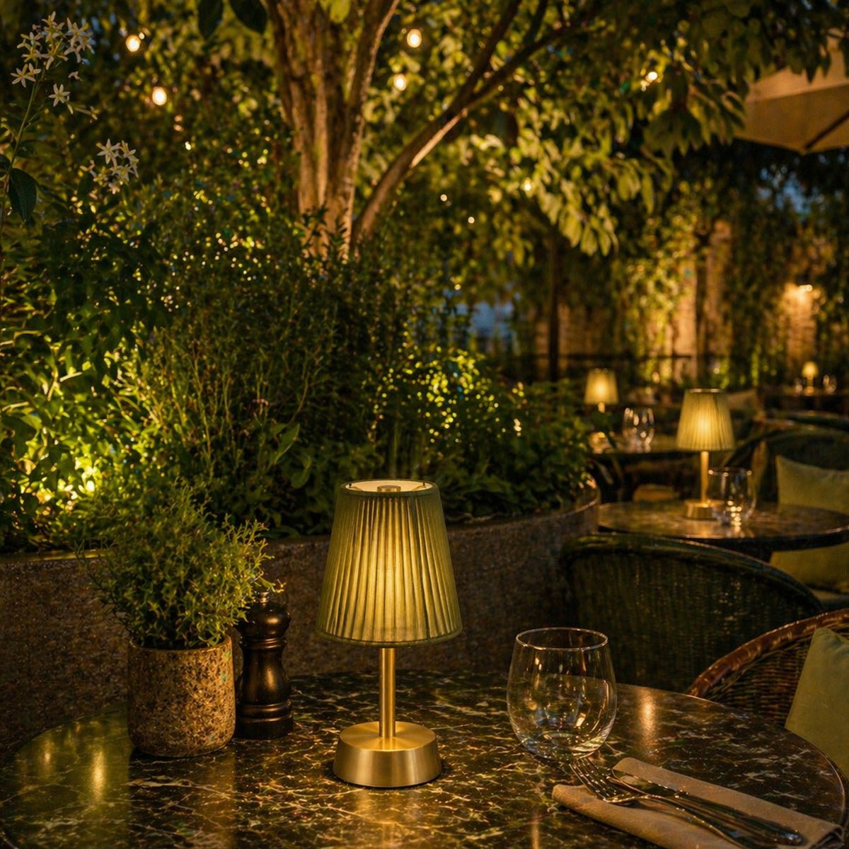 Evening outdoor setting with rechargeable table lamp, and glasses in a garden.