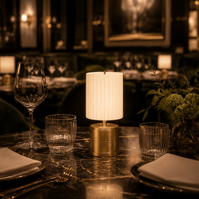 Dining table setting with a rechargeable cordless lamp, glasses, and plates in a dimly lit restaurant.