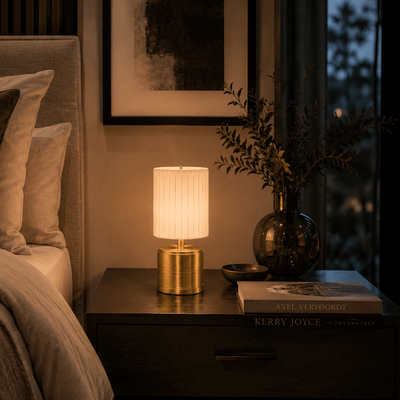 Rechargeable lamp on a bedside table with a book and plant in a dimly lit room.