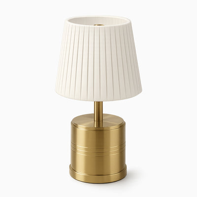 Cordless table lamp with a ivory pleated shade and brass base on a white background