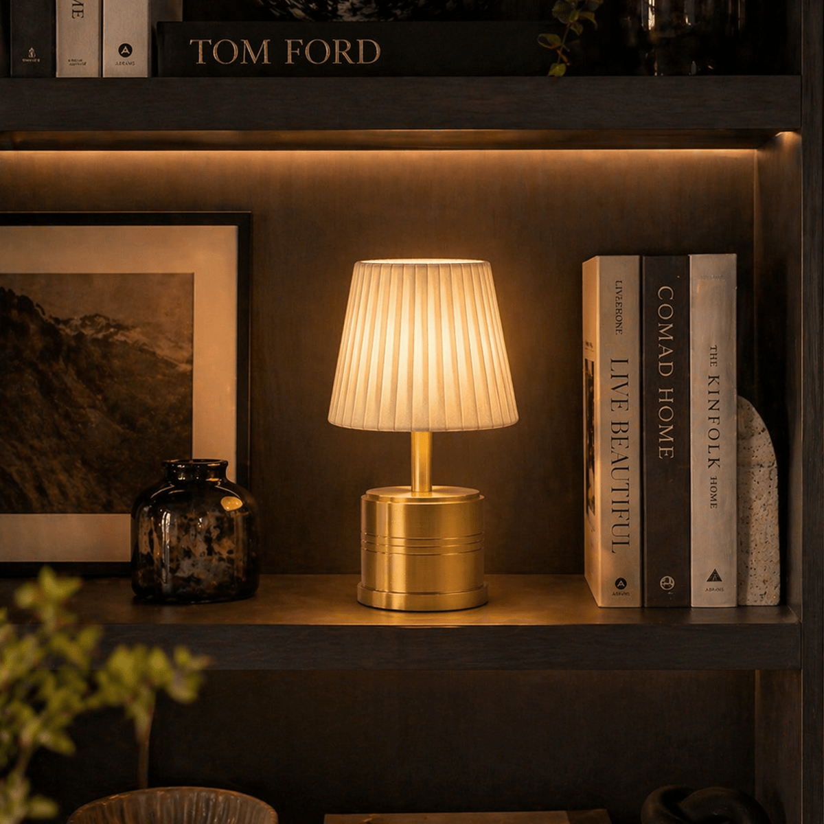 Brass rechargeable table lamp on a shelf with books and decor items in a warm setting