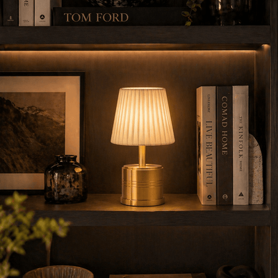 Brass rechargeable table lamp on a shelf with books and decor items in a warm setting