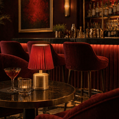 Luxurious bar setting with red velvet chairs, a rechargeable table lamp, and drinks.