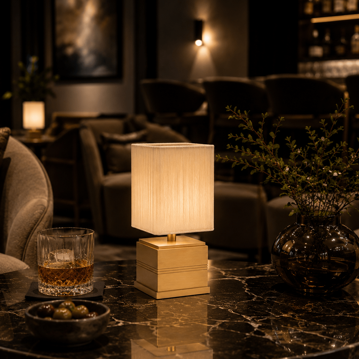 Decorative rechargeable lamp on a marble surface with a glass of whiskey and a bowl of snacks in a dimly lit room.