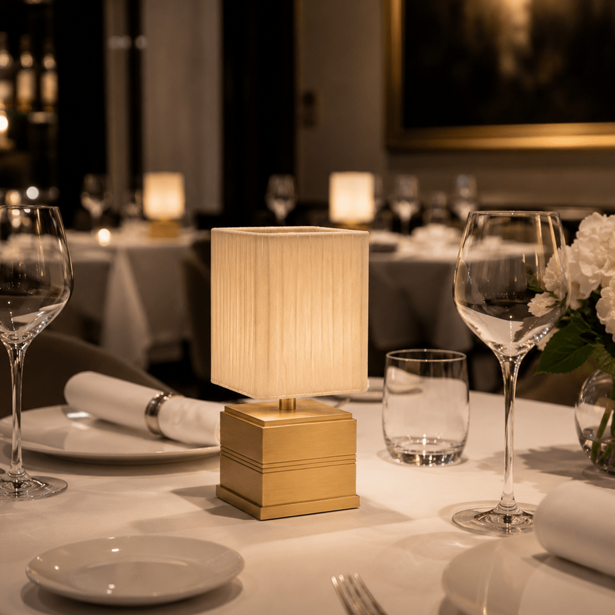 Elegant table setting with a rechargeable lamp, wine glasses, and plates in a restaurant.