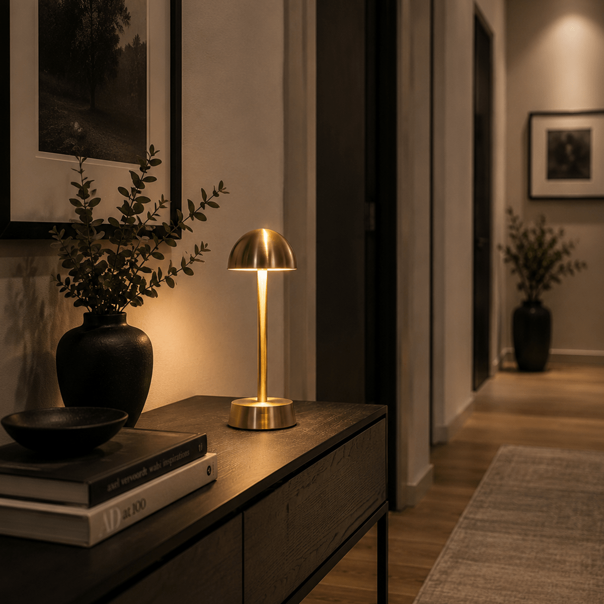 Modern interior with a gold rechargeable cordless lamp, books, and a vase on a wooden surface.
