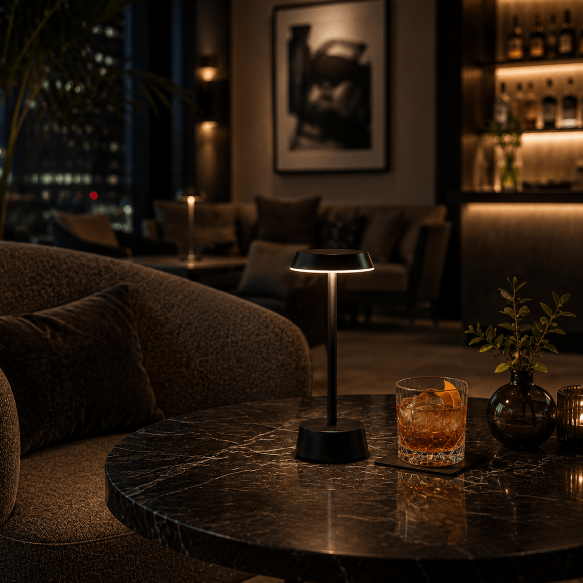 Dark, cozy bar setting with a cocktail and a Black rechargeable lamp on a marble table