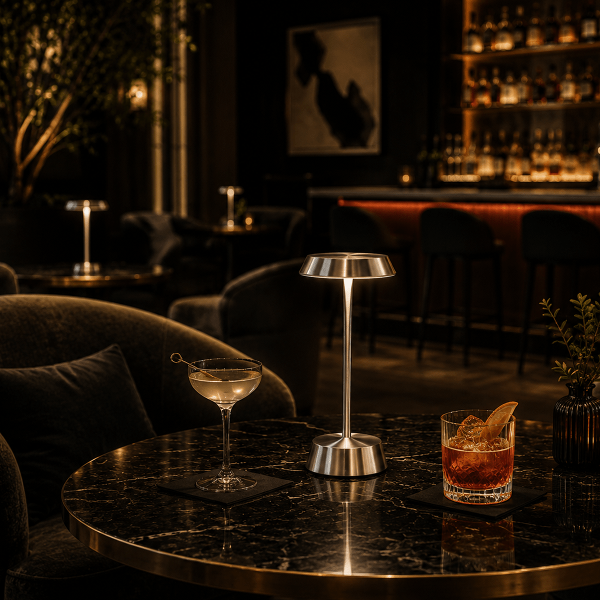 Dark-themed bar with cocktails and a silver rechargeable lamp on a table