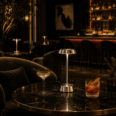 Dark-themed bar with cocktails and a silver rechargeable lamp on a table