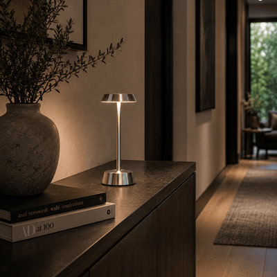 Modern rechargeable table lamp on a wooden surface with a vase and books in a cozy room.
